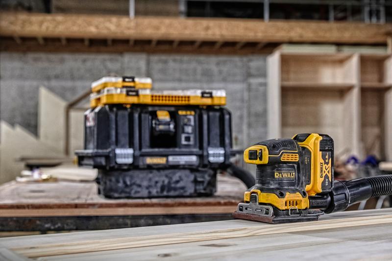 DEWALT draadloze schuurmachine op hout, opslagbox op de achtergrond in een werkplaats.