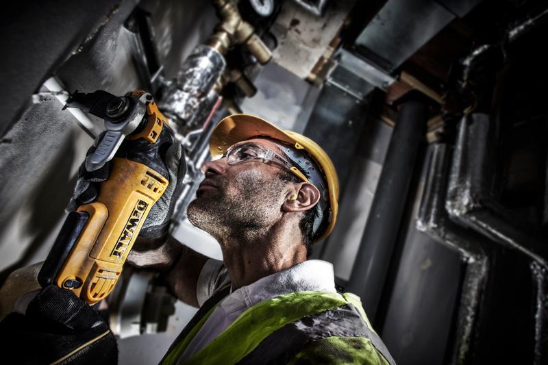 Werknemer gebruikt DEWALT DWE315 gereedschap om een pijp te snijden, draagt helm en vest op werkplek.